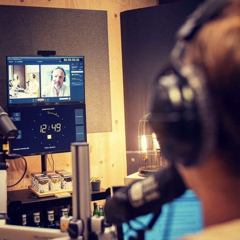 Over-the-shoulder view in a podcast studio: video session on top, OnAirScreen clock on the lower monitor