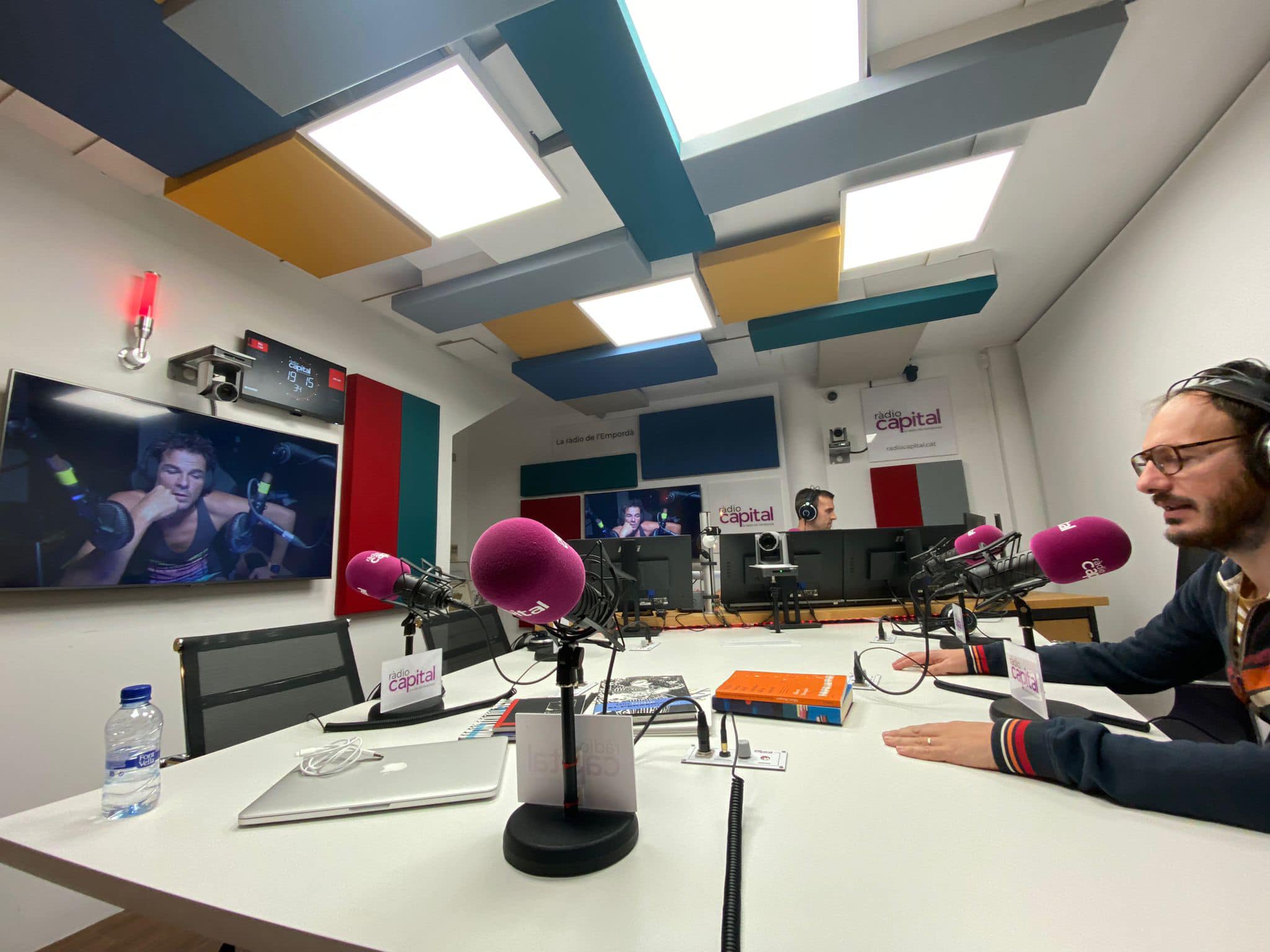 Talk studio with a white table, broadcast microphones, and a red on-air lamp on the wall