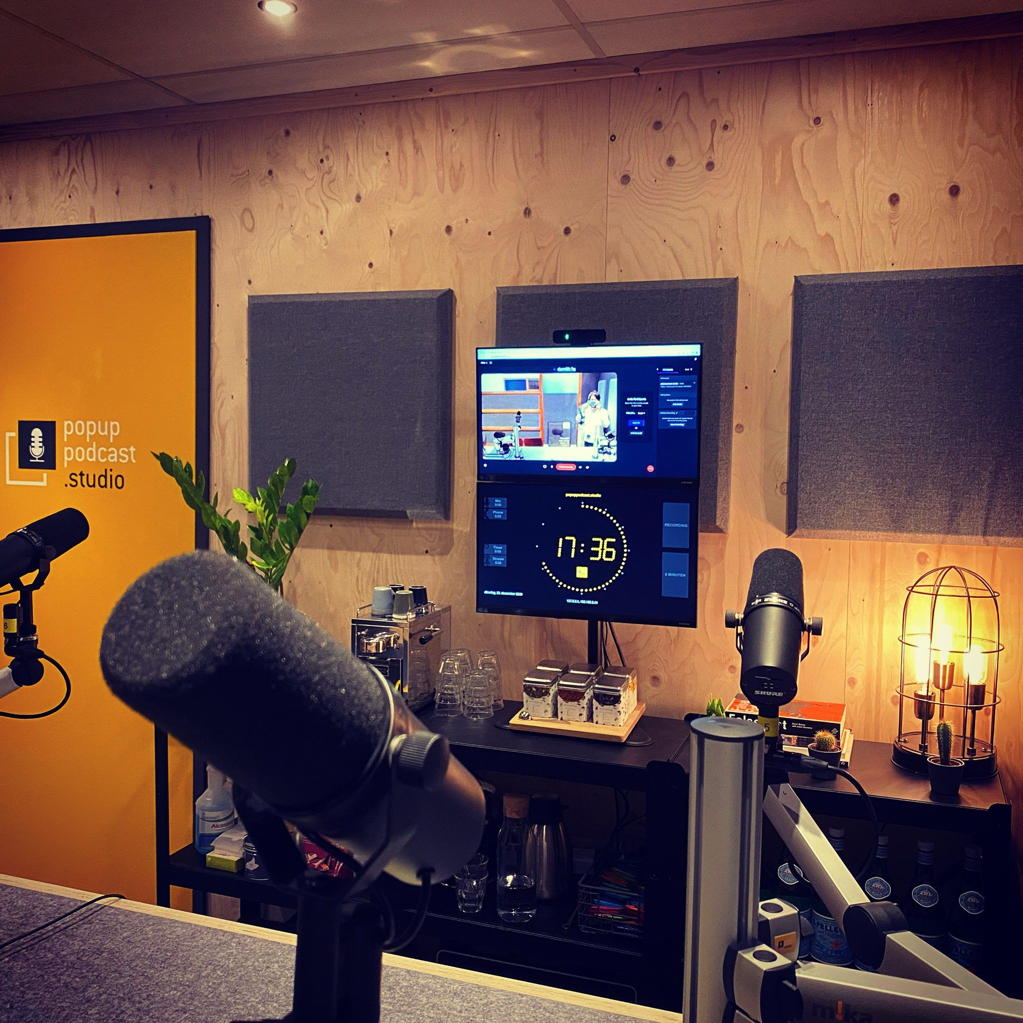 Podcast studio with broadcast microphones, wood-panelled wall, and OnAirScreen clock on the lower monitor