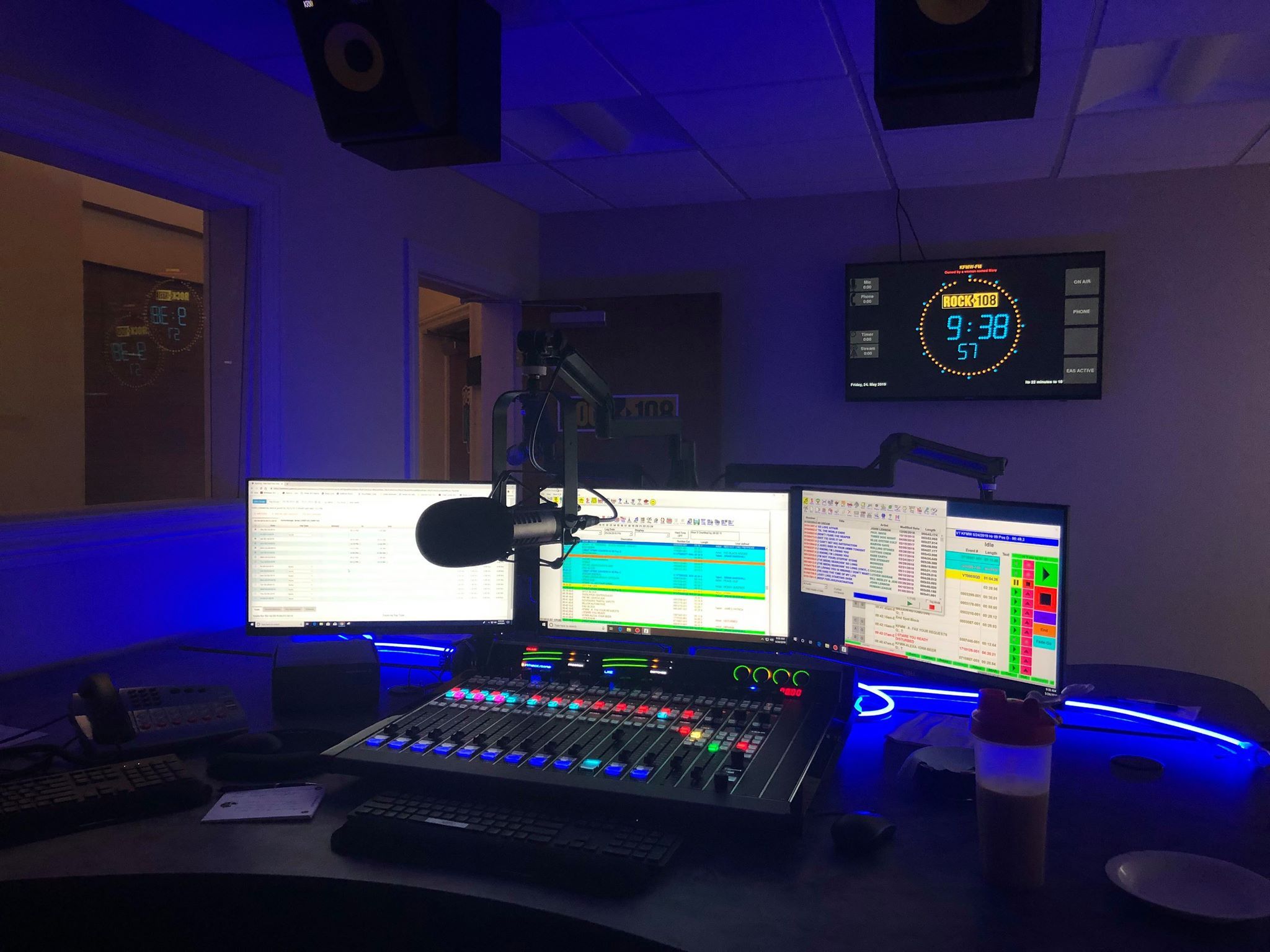 Radio studio with digital mixer, three monitors, and OnAirScreen as a wall clock with station logo